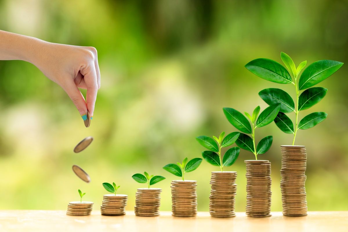 An asian girl hand holding a coin to invest. There a pile of coins as return or earning on investment concept. It is for retirement and finance concept.